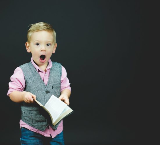 boy wearing gray vest and pink dress shirt holding book